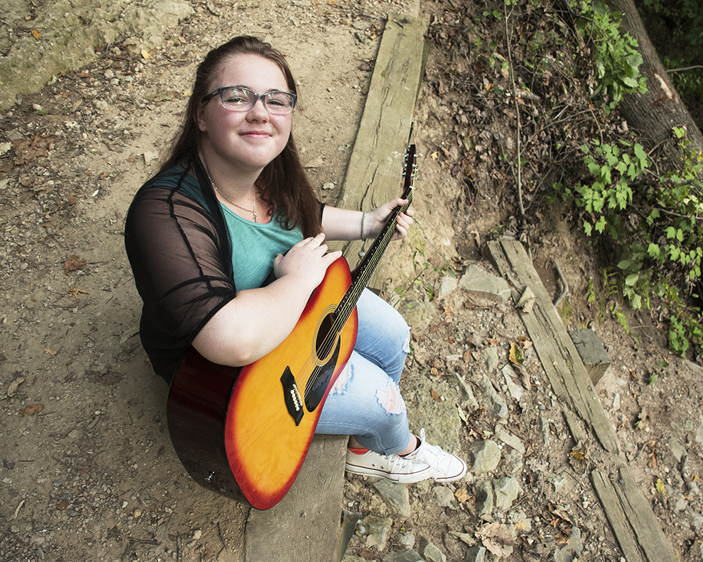 Young female posing for senior picture on location with guitar